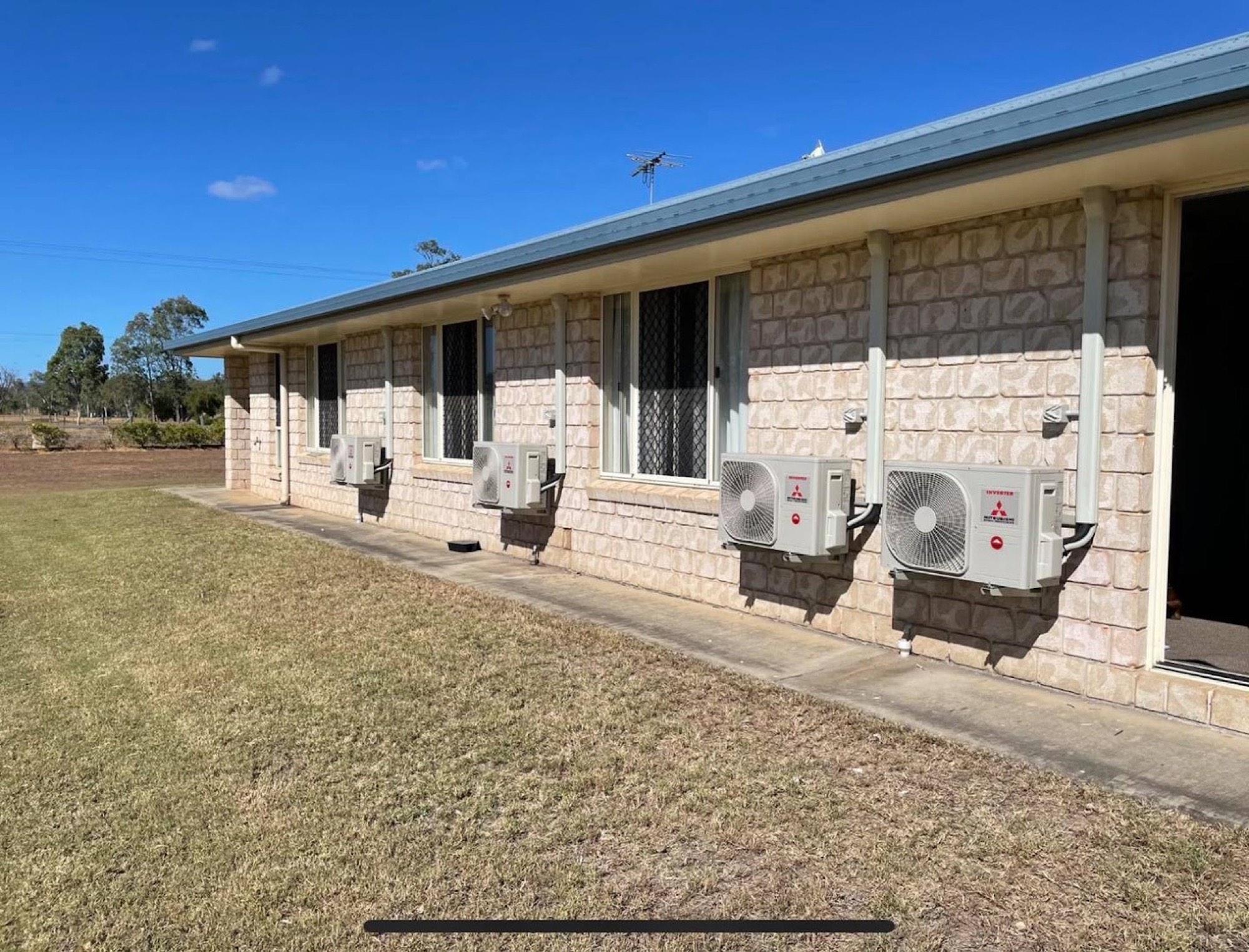 Four split system condensers installed along the wall of a brick building