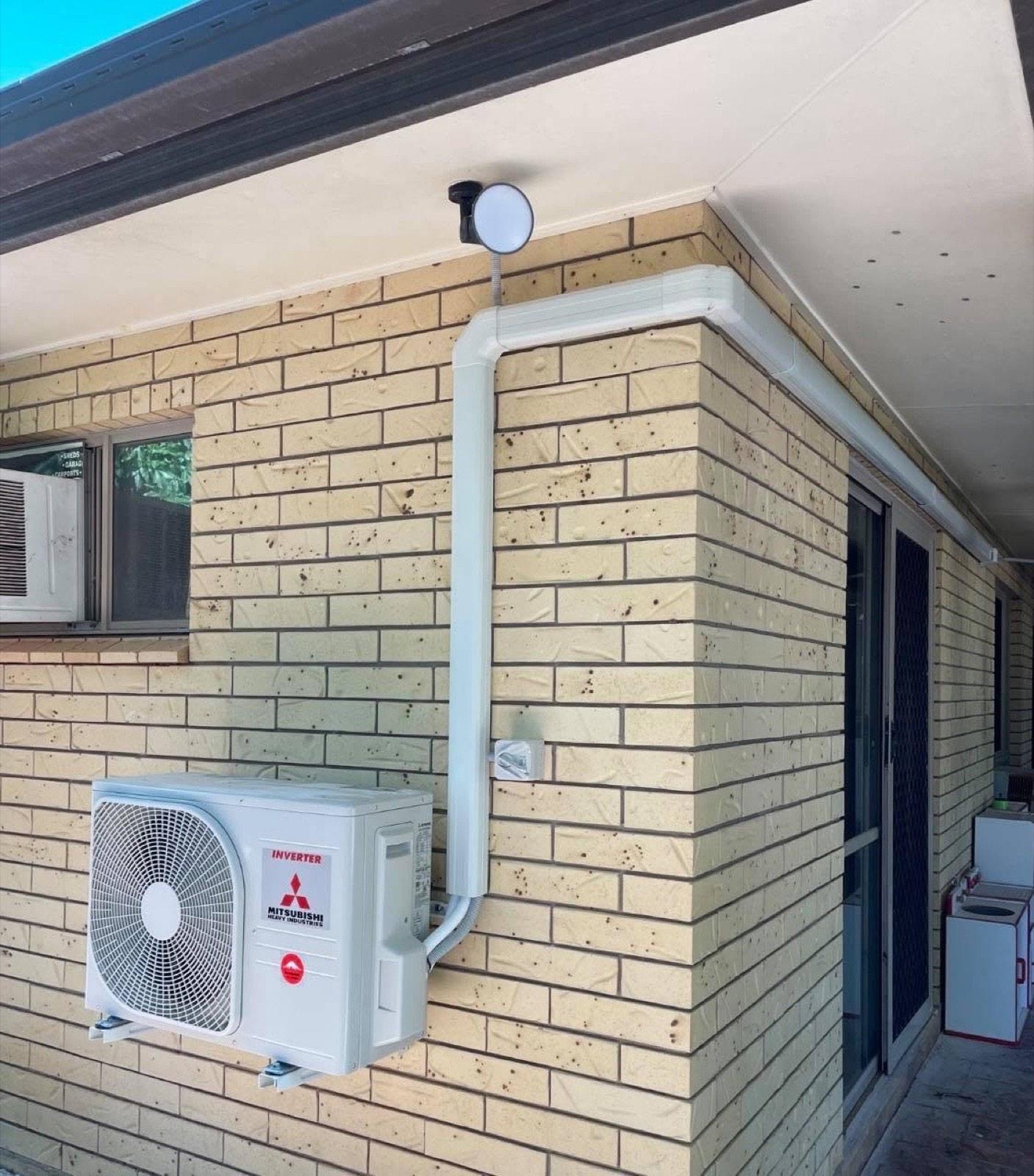 A split system condenser mounted on a brick wall with neat conduit run to the eave