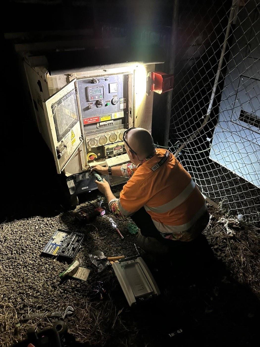 An electrician working inside an open switchboard cabinet under work light