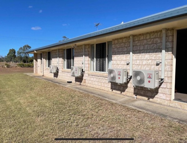 Four split system condensers installed along the wall of a brick building