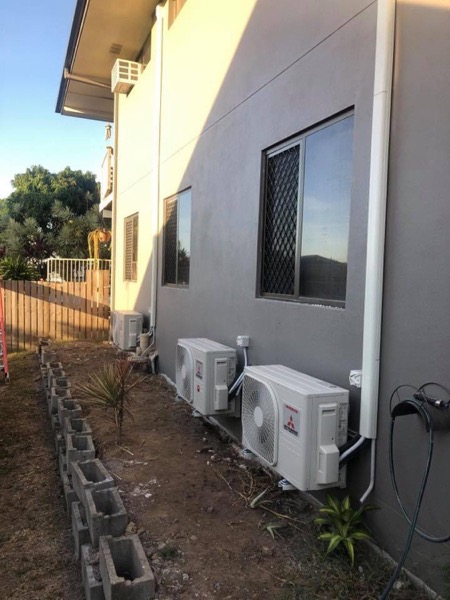 Two split system condensers installed beside a rendered house