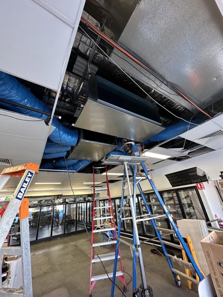 Ceiling ductwork and framing in a shop being fitted out, with a ladder in place