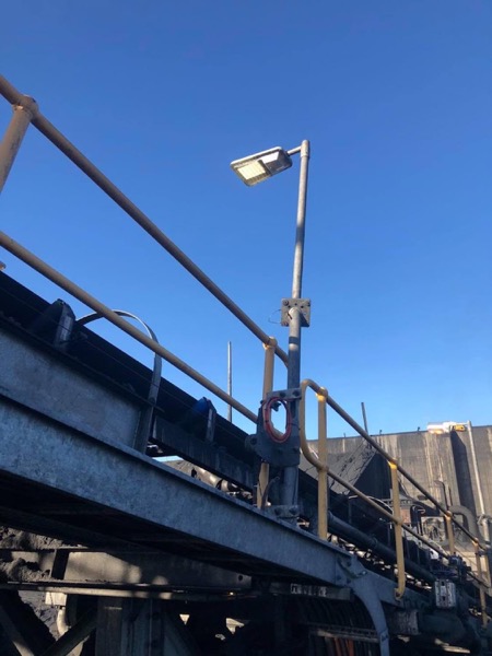 A street light head mounted on a steel pole against a clear sky