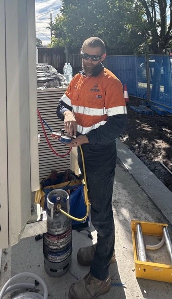 A tradesman brazing pipework beside a gas bottle at the side of a building
