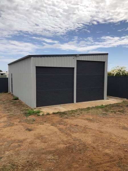 A completed Colorbond shed with two roller doors on a cleared block