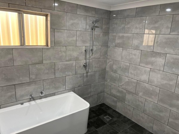 A finished bathroom with a freestanding bath and large format tiles